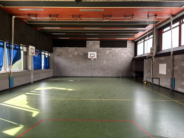 De sporthal met basketbalringen en klimtouwen